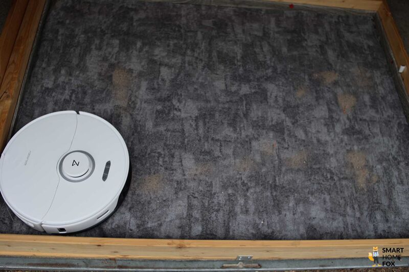 Roborock S8 Pro Ultra reinigt beim Saugtest Sand auf einem Teppichboden.
